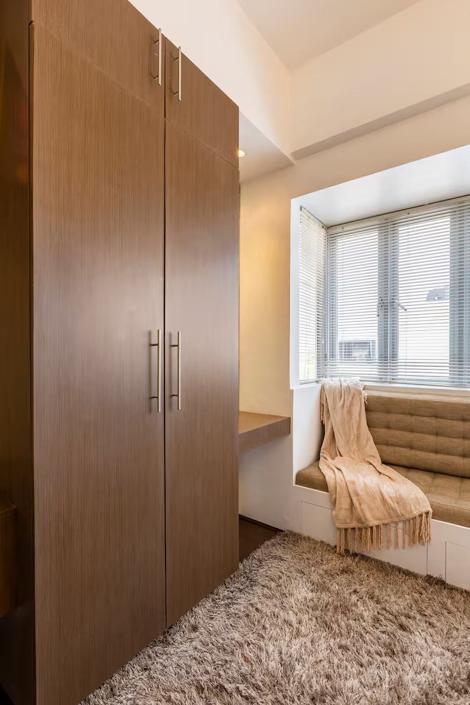 A cushioned window seat with a throw draped over it, next to the wardrobe